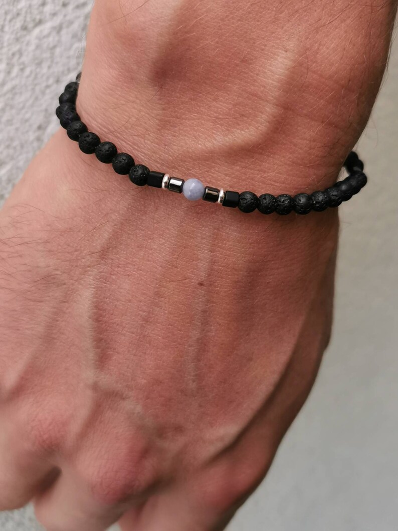 May include: A black lava rock bracelet with a single light blue gemstone bead and silver accents.