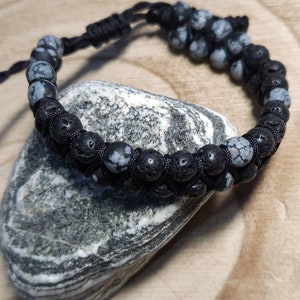Könnte beinhalten: Schwarzes und graues Perlenarmband mit schwarzem Band. Das Armband besteht aus Lava- und Schneeflocken-Obsidianperlen.