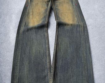 May include: Faded blue denim jeans with a wide leg design. The jeans have a distressed look with lighter patches on the thighs and knees. Features include a button closure, belt loops, and decorative stitching.