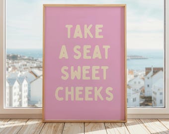 Może przedstawiać: Różowy wydruk w ramie z tekstem "TAKE A SEAT SWEET CHEEKS" w jasnożółtym kolorze.