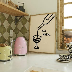 May include: A framed print with a black and white illustration of a wine bottle pouring into a glass. The text "SAY WHEN..." is written below the illustration.