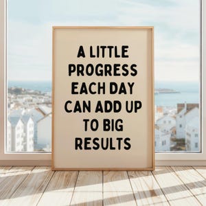 Może przedstawiać: Beżowy plakat w drewnianej ramie z motywacyjnym cytatem. Cytat brzmi "A little progress each day can add up to big results".