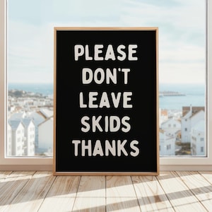 May include: A black framed sign with white text that reads "PLEASE DON'T LEAVE SKIDS THANKS". The sign is in front of a window with a view of a city and ocean.