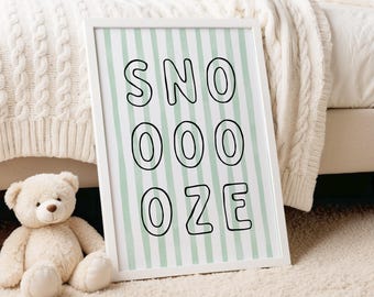 May include: A framed print with the word "SNOOOZE" in black letters on a light green and white striped background. A white teddy bear sits on a cream-colored rug next to the frame. The frame is white.