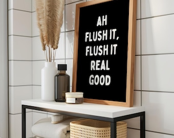 May include: A framed black sign with the text "AH FLUSH IT, FLUSH IT REAL GOOD" in white. The sign is in a bathroom setting, with a white shelf holding a vase with dried plants, a brown bottle, a small jar, and a woven basket.