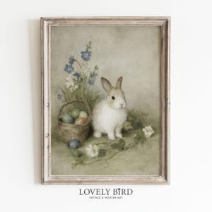 Könnte beinhalten: Gerahmter Kunstdruck im Vintage-Stil mit einem weißen und braunen Hasen, einem Korb mit Ostereiern und blauen Blumen. Das Kunstwerk hat eine weiche, gedämpfte Farbpalette und den Text "LOVELY BIRD VINTAGE & MODERN ART" am unteren Rand.