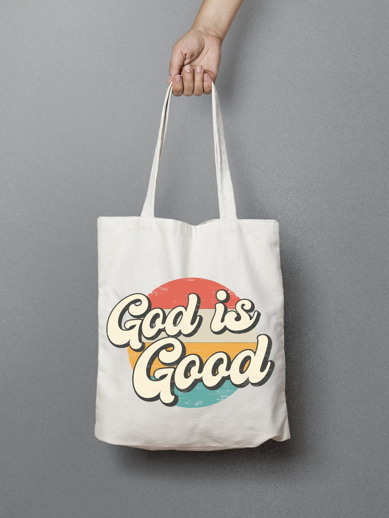 May include: White canvas tote bag with a retro-style graphic of a red, orange, yellow, and blue circle with the text "God is Good" in a vintage font.