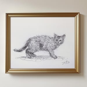 May include: A framed artwork featuring a pen and ink drawing of a cat. The cat is depicted in a scribbled style, with a gold-colored frame. The artwork is mounted on a white background.