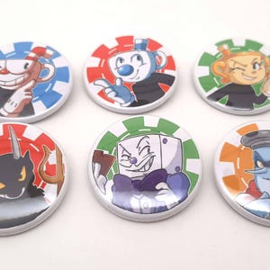 Może przedstawiać: Sześć okrągłych przypinek z postaciami z gry wideo Cuphead. Każda przypinka ma białe tło z kolorową obwódką i ilustracją postaci z kreskówek. Postacie to m.in. Cuphead, Mugman i Diabeł.