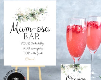 May include: A printable sign for a mimosa bar with greenery and gold accents. The sign reads "Mum-osa Bar" and includes instructions for making mimosas: "POUR the bubbly, ADD some juice, TOP with fruit, Cheers!" There is a smaller sign that reads "Orange".