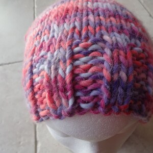 May include: A pink, purple and white knitted hat with a fluffy texture.