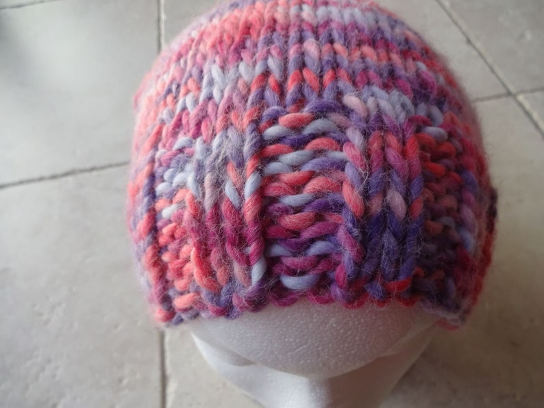May include: A pink, purple and white knitted hat with a fluffy texture.