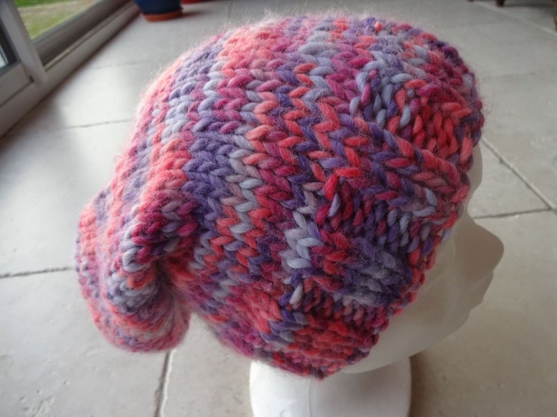 May include: A pink and purple knitted beanie hat with a slouchy fit.