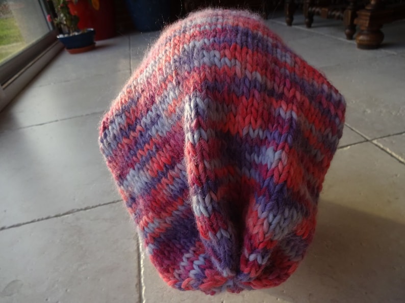 May include: A pink and purple striped knitted hat. The hat is made of soft yarn and has a slouchy fit.