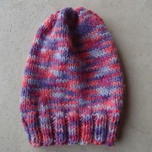 May include: A knitted hat with a striped pattern in shades of pink, purple, and white.