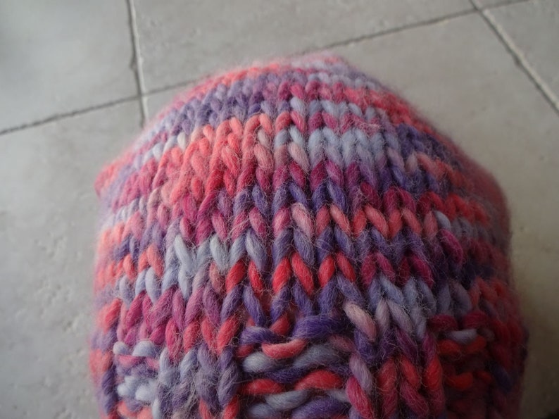 May include: A close-up of a knitted hat in a pink, purple and white colour scheme. The hat is made from a soft, fuzzy yarn.