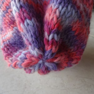 May include: Close-up of a knitted hat with a pink, purple and white colour pattern.