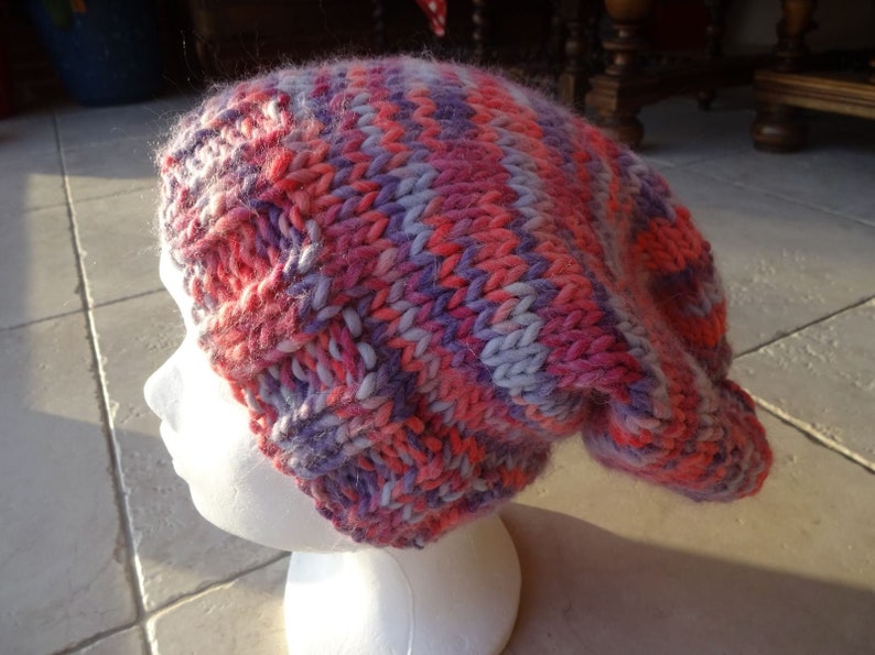 May include: A pink, purple and white knitted beanie hat with a slouchy fit.