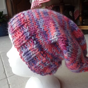 May include: A pink, purple and white knitted beanie hat with a slouchy fit.