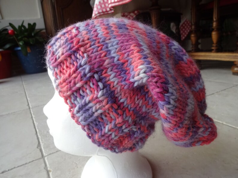 May include: A pink, purple and white knitted beanie hat with a slouchy fit.