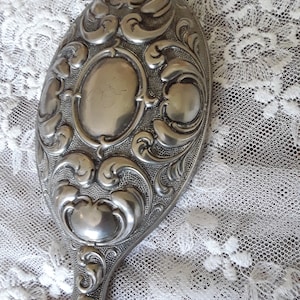 Peut inclure: Un miroir de poche en argent avec un motif gravé orné. Le miroir est de forme ovale et possède un manche.