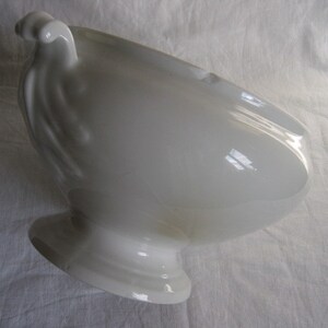 Puede incluir: Taz&oacute;n de servir de porcelana blanca con un asa decorativa. El taz&oacute;n tiene una forma redondeada y una base de pedestal.