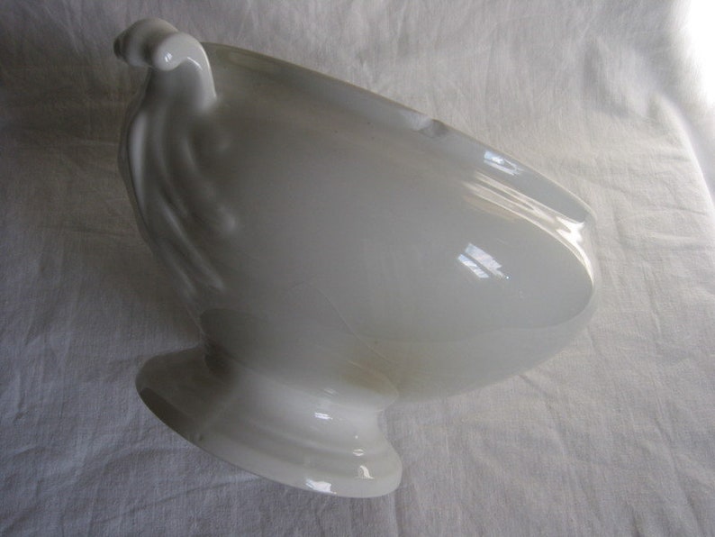 Puede incluir: Taz&oacute;n de servir de porcelana blanca con un asa decorativa. El taz&oacute;n tiene una forma redondeada y una base de pedestal.