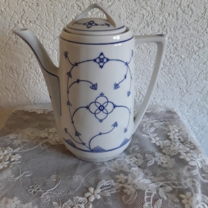 Può includere: Una caffettiera in ceramica bianca con un motivo floreale blu e bianco. La caffettiera ha un coperchio e un beccuccio.