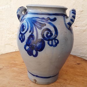 May include: A blue and white ceramic crock with two handles. The crock has a floral design painted on the side.