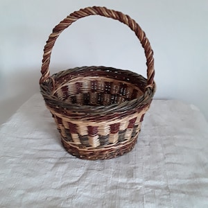 May include: A woven basket with a brown, green and cream chequered pattern. The basket has a twisted rope handle.