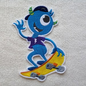 Könnte beinhalten: Blauer Monster mit einem Auge, das ein lila Shirt und eine schwarze Baseballkappe trägt, fährt Skateboard auf einem gelben Skateboard mit schwarzen Rädern.