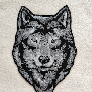 Könnte beinhalten: Ein gestickter Wolfskopf-Patch in Schwarz und Weiß. Die Augen des Wolfes sind weiß und das Fell ist mit weißen Stichen detailliert.