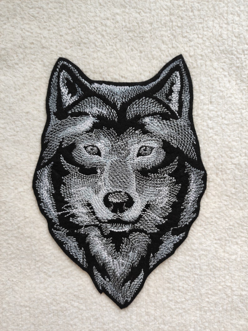 May include: A black and white embroidered wolf head patch. The wolf's eyes are white and the fur is detailed with white stitching.