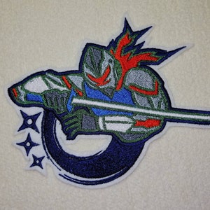 Könnte beinhalten: Gestickter Aufnäher mit einem stilisierten Krieger mit Helm und Schwert. Das Design verwendet Blau, Grün, Rot und Silber, mit drei blauen Ninja-Sternen. Der Krieger ist vor einem dunkelblauen, geschwungenen Hintergrund platziert.