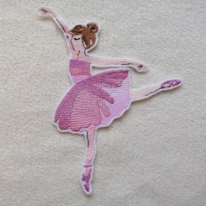 Könnte beinhalten: Rosa gestickter Ballerina-Aufnäher mit einem braunen Dutt und einem rosa Tutu. Die Ballerina ist in einer Tanzpose mit einem ausgestreckten Bein.