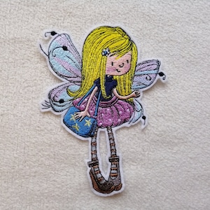 Könnte beinhalten: Ein gestickter Aufnäher mit einer Zeichentrickfigur mit langem gelben Haar, einem dunkelblauen Oberteil und einem violetten Rock mit Punkten. Die Figur hat schillernde Flügel, gestreifte Leggings, braune Schuhe und eine blaue Tasche mit gelben Sternen.