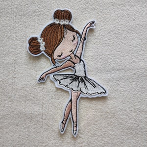 Könnte beinhalten: Ein gestickter Bügelaufkleber mit einer Ballerina mit braunen Haaren, einem weißen Tutu und rosa Schuhen.