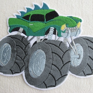Könnte beinhalten: Grüne Monstertruck-Stickerei mit großen schwarzen Reifen auf weißem Hintergrund.