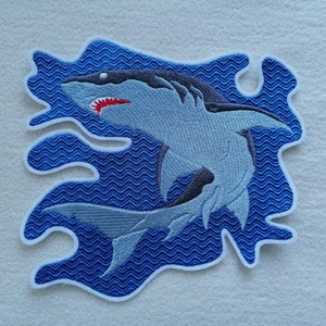 Könnte beinhalten: Gestickter Bügel-Patch mit einem blauen Hai mit weißen Zähnen und rotem Zahnfleisch, der in einem blauen, wellenförmigen Wasserdesign schwimmt.
