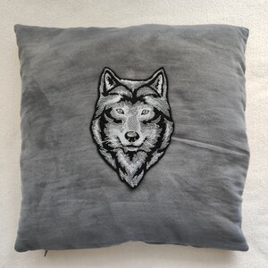 May include: A gray throw pillow with a black and white embroidered wolf head design.
