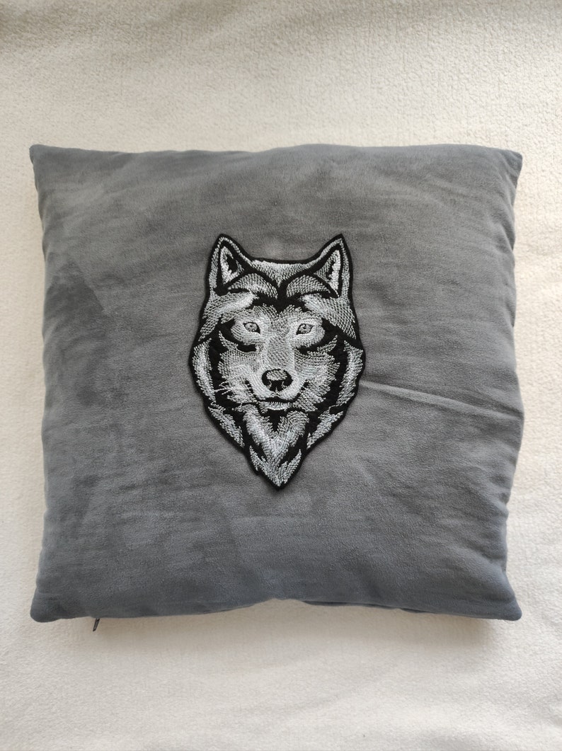 May include: A gray throw pillow with a black and white embroidered wolf head design.