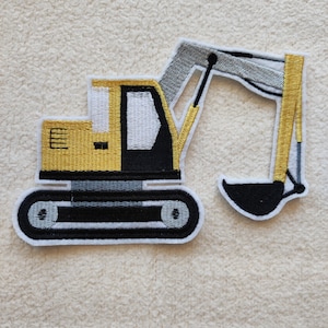 Könnte beinhalten: Gelber und schwarzer gestickter Bügelaufkleber einer Baggerschaufel mit grauem Arm und schwarzem Eimer.
