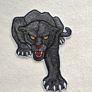 Könnte beinhalten: Schwarzer gestickter Panther-Patch mit weißen Krallen und gelben Augen. Der Panther knurrt mit einem roten Maul.
