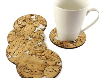 May include: A collection of round cork coasters with a natural, textured finish. A white mug rests on one of the coasters. The coasters are light brown with white details, designed to protect surfaces from heat and moisture.