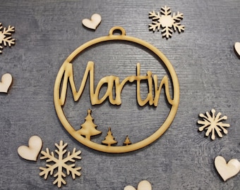 May include: A circular wooden ornament featuring the name Martin in cursive script, with three small pine trees at the bottom. The ornament is surrounded by several small wooden snowflake cutouts and heart-shaped wooden pieces.