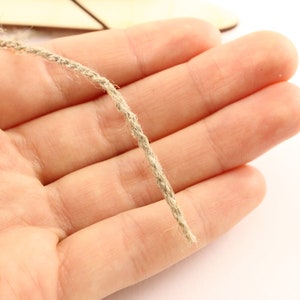 May include: A close-up of a natural twine string, held in a hand, against a white background.