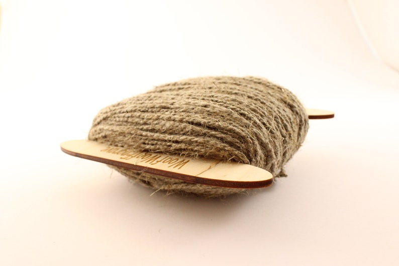 May include: A ball of natural brown twine wrapped around two wooden dowels with the text "Wool Winding" printed on the dowels.