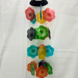 Puede incluir: Un colorido móvil de viento con adornos en forma de flor en tonos rojos, amarillos, verdes, azules y naranjas. El móvil cuelga de una parte superior negra en forma de cúpula. Los adornos florales están unidos con una cuerda transparente.
