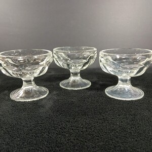 May include: Three clear glass dessert bowls with a wide, shallow basin and a short, sturdy pedestal base. Each bowl features a subtle, rippled texture along the exterior rim, providing a decorative element to the otherwise smooth, transparent glass.