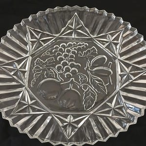 May include: A clear glass serving plate with a scalloped edge and a raised design of grapes and leaves in the center.